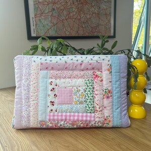 May include: A pink and blue patchwork quilt-style zippered pouch with a variety of floral and geometric patterns.