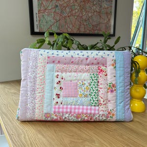 May include: A pink and blue patchwork fabric zippered pouch with a quilted design. The pouch is made of various floral and geometric patterns.