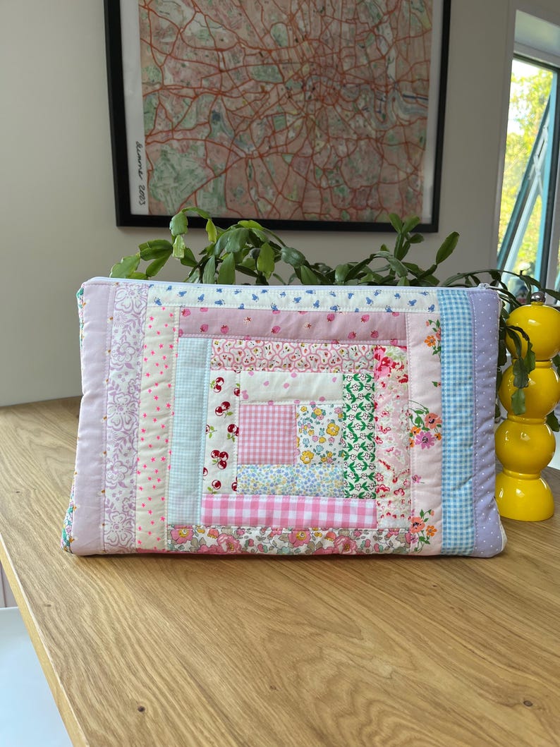 May include: A pink and blue patchwork fabric zippered pouch with a quilted design. The pouch is made of various floral and geometric patterns.