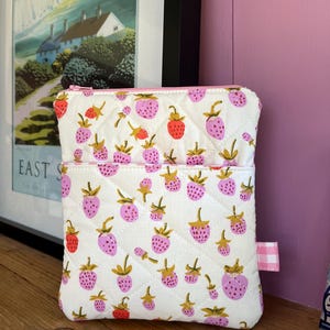 May include: Two white quilted pouches with a strawberry design. The strawberries are pink and red with gold stems and leaves. The pouches have pink zips and a small pink and white gingham tag.