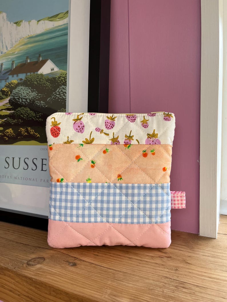 Pu&ograve; includere: Un astuccio trapuntato con un design patchwork. La sezione superiore presenta uno sfondo bianco con fragole rosa. La sezione centrale &egrave; color pesca con piccoli frutti arancioni. La sezione inferiore &egrave; a quadretti blu e la base &egrave; rosa.