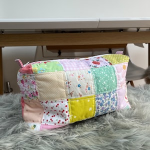 Może przedstawiać: Kosmetyczka z tkaniny patchworkowej z zamkiem błyskawicznym. Torebka wykonana jest z różnych wzorów kwiatowych i geometrycznych w kolorze różowym, zielonym, żółtym i białym.