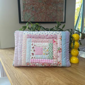 May include: A pink and white patchwork quilt-style zippered pouch with a variety of floral and geometric patterns.