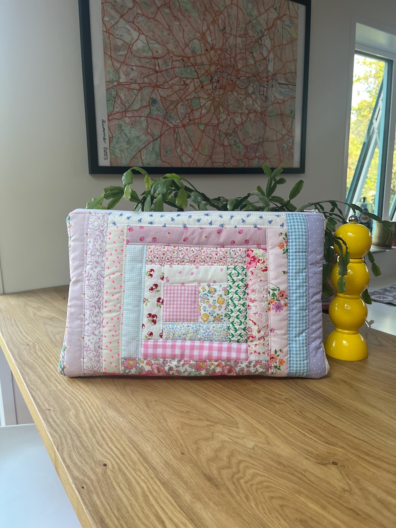 May include: A pink and white patchwork quilt-style zippered pouch with a variety of floral and geometric patterns.