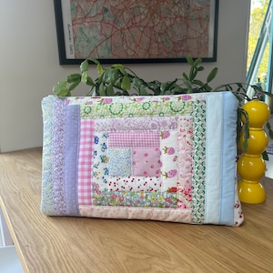 May include: A patchwork quilt-style zippered pouch with a variety of floral and geometric patterns in shades of pink, blue, and green.