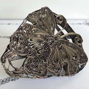 May include: An antique metal stamp with a butterfly design. The stamp has intricate cut-out patterns and a dark, aged finish. The butterfly's wings and body are clearly defined, showcasing the craftsmanship. It is likely used for textile printing or decorative purposes, possibly for fabric.