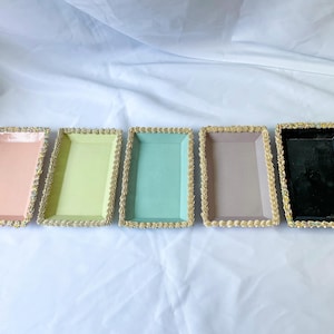 May include: Five rectangular trays with gold trim. The trays are in the colors pink, green, blue, gray, and black.