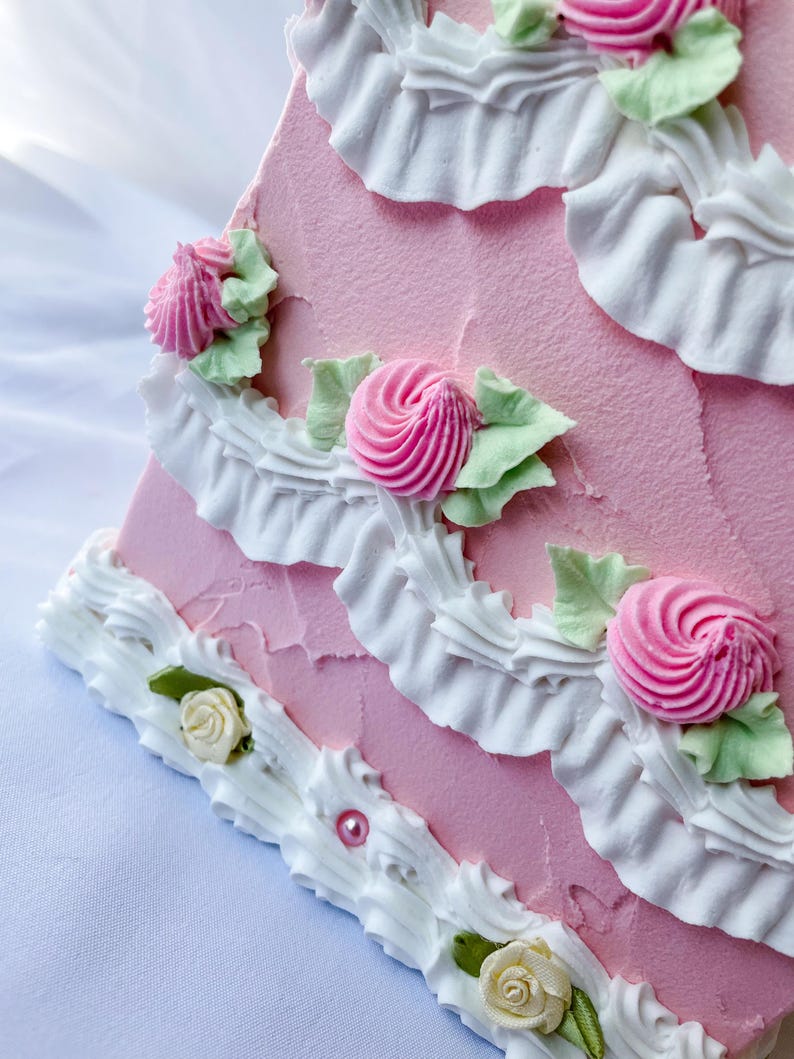 May include: A pink cake decorated with white frosting and pink and white flowers. The cake is layered and has a ruffled edge.