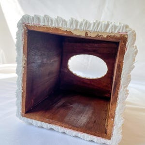 May include: White tissue box cover with a decorative, ruffled edge. The cover is made of a textured material and has a rectangular opening for tissues.