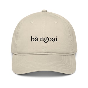 May include: A beige baseball cap with black embroidered text that reads "bà ngoại".