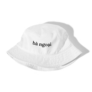 Puede incluir: Sombrero de pescador blanco con el texto "bà ngoai" bordado en la parte delantera.
