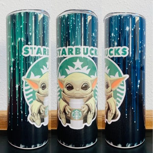 May include: A stainless steel tumbler featuring a black and green Starbucks logo and a cartoon image of a green alien holding a Starbucks cup. The background is a dark blue with white stars and streaks of light.