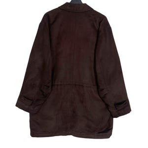 May include: A dark brown suede jacket with a collared neckline, long sleeves, and two front pockets. The jacket has a button closure and a tailored fit. The garment is hanging on a black hanger.