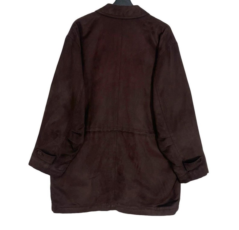 May include: A dark brown suede jacket with a collared neckline, long sleeves, and two front pockets. The jacket has a button closure and a tailored fit. The garment is hanging on a black hanger.