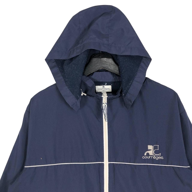 Puede incluir: Chaqueta con capucha azul marino con cremallera y ribetes blancos. El logotipo "courr&egrave;ges" es de color beige claro en el pecho. La capucha est&aacute; forrada con un material azul m&aacute;s oscuro. Una prenda de vestir exterior cl&aacute;sica.