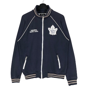 May include: Navy blue zip-up jacket with white piping and the text "TORONTO MAPLE LEAFS". Features a white maple leaf logo. The jacket has a ribbed collar, cuffs, and hem with brown and white stripes.