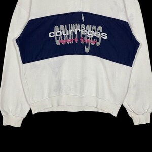 Puede incluir: Sudadera blanca con un panel azul marino en el pecho. El panel presenta el texto bordado "courreges sport futur" en plata y rosa. La sudadera tiene cierre de cremallera de un cuarto y mangas largas.