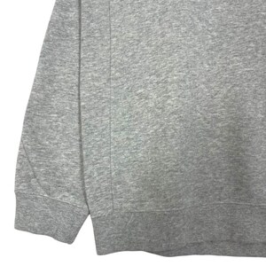 May include: A close-up of a grey sweatshirt. The image shows the sleeve and lower portion of the garment, with a ribbed cuff and hem. The fabric has a textured appearance, and a vertical seam is visible.