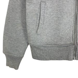 May include: Close-up of a gray zip-up hoodie. The hoodie features a front pocket, ribbed cuffs, and a ribbed hem. The zipper runs down the front of the garment. The fabric appears to be a soft, medium-weight material.