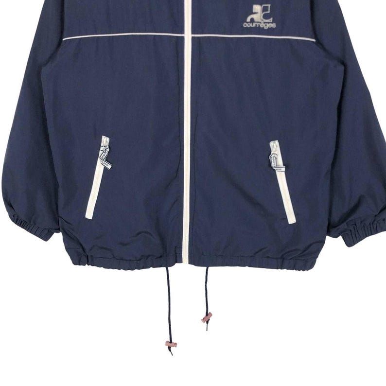 Puede incluir: Chaqueta azul marino con cremallera, ribetes blancos y el logo de Courreges. La chaqueta tiene un cord&oacute;n en la parte inferior y dos bolsillos delanteros. La chaqueta est&aacute; hecha de un material ligero.