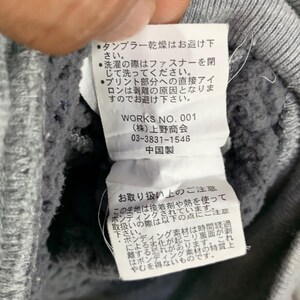 May include: Close-up of a gray sweatshirt with a white tag attached. The tag has Japanese text and the words "WORKS NO. 001". The sweatshirt has a textured interior.