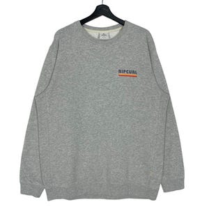 May include: A grey sweatshirt featuring the word "RIPCURL" in orange and white across the chest. The long-sleeved crew neck shirt is made of a soft material.