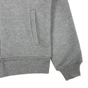 May include: Close-up of a gray zip-up sweatshirt. The sweatshirt features a front pocket and ribbed cuffs and hem. The fabric appears to be a soft, medium-weight material. The sleeve is visible, showing the cuff detail.
