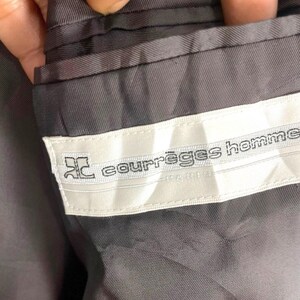 May include: Close-up of the interior of a gray suit jacket. A white label with the text "courr&egrave;ges homme" is sewn into the lining. The label also features a stylized logo.