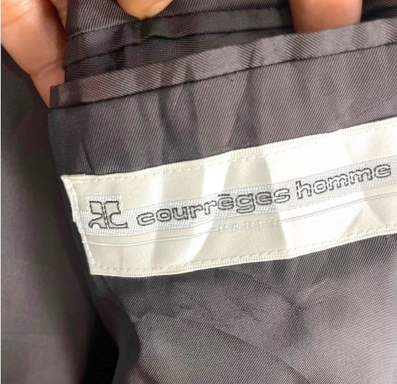 May include: Close-up of the interior of a gray suit jacket. A white label with the text "courr&egrave;ges homme" is sewn into the lining. The label also features a stylized logo.