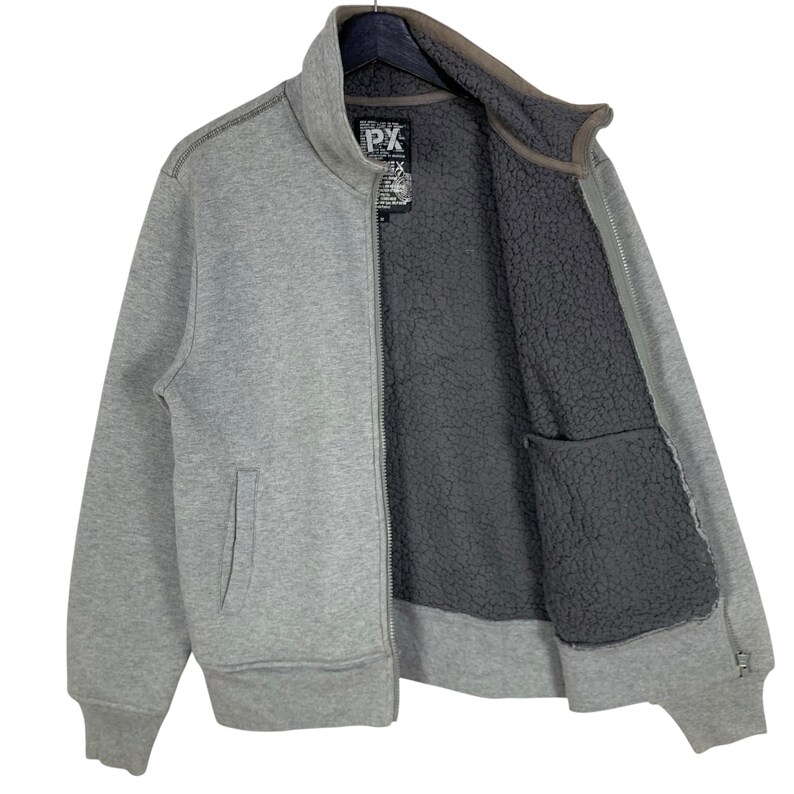 May include: A gray zip-up jacket with a high collar and a dark gray, fuzzy interior. The jacket has a front pocket and a small tag with the letters "PX". The jacket is hanging on a black hanger.
