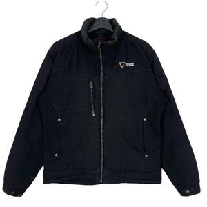 Puede incluir: Chaqueta negra acolchada con cierre de cremallera completo, cuello alzado y un pequeño bolsillo en el pecho. La chaqueta tiene el texto "BOUKEN HOLDINGS" y un logotipo triangular en el pecho.