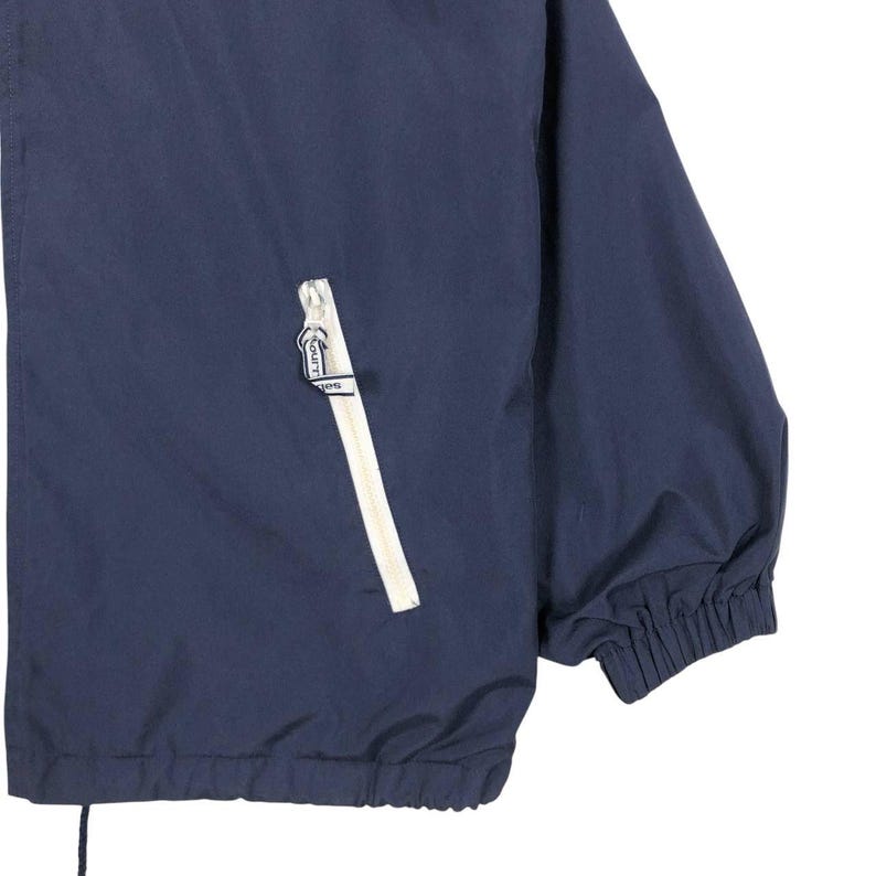 Puede incluir: Chaqueta azul marino con cremallera y ribete de bolsillo blancos. La chaqueta tiene un cord&oacute;n en la parte inferior y pu&ntilde;os el&aacute;sticos. El tirador de la cremallera tiene la palabra "Lino" impresa. La chaqueta es de material ligero.