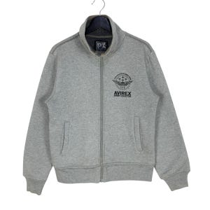 May include: A gray zip-up sweatshirt with a stand-up collar. The sweatshirt features the text "PX" on the collar and a graphic with the text "AVIREX ARMY AVIATOR" on the chest. It has two front pockets.