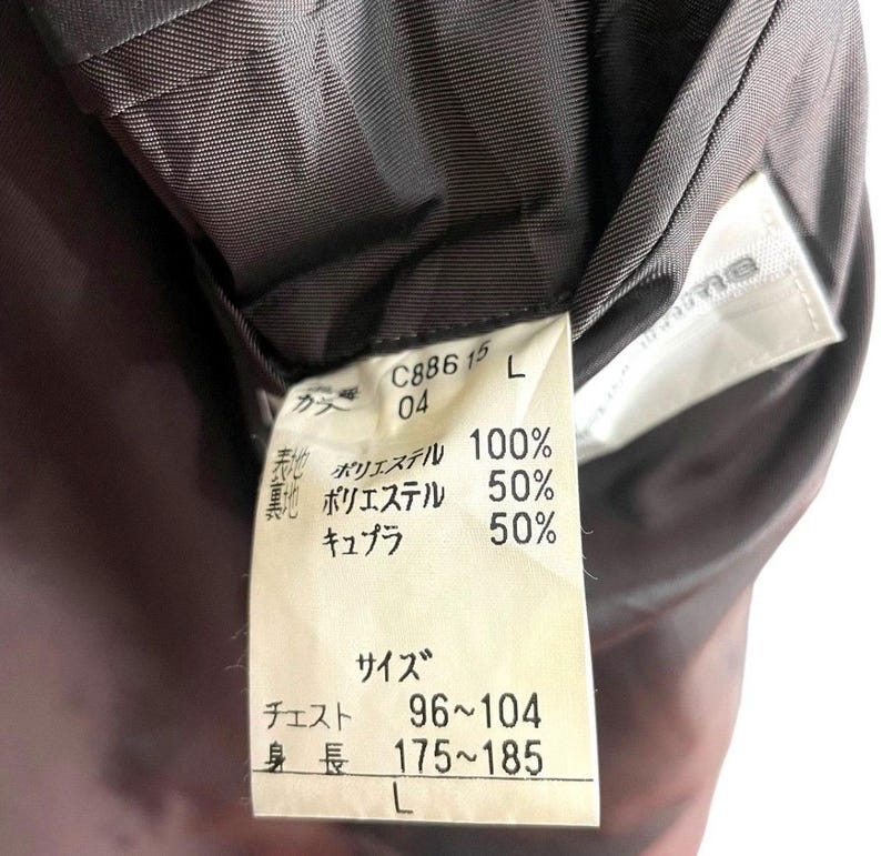 May include: Close-up of a garment tag with Japanese text. The tag is white with black text and includes fabric composition percentages. The tag also lists chest and height measurements, and the size is L.