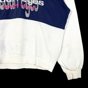 Puede incluir: Sudadera blanca con un panel azul marino en el pecho. El panel presenta el texto "courreges sport futur" en letras plateadas y rosas. La sudadera tiene pu&ntilde;os y dobladillo de canal&eacute;.