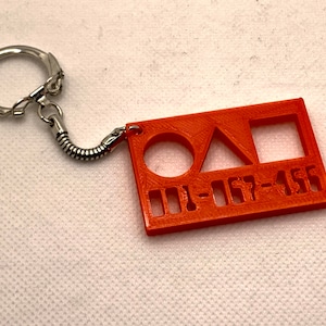May include: Orange plastic keyring with a circle, triangle, and square cutout. The keyring also has the text "001-157-455" printed on it.