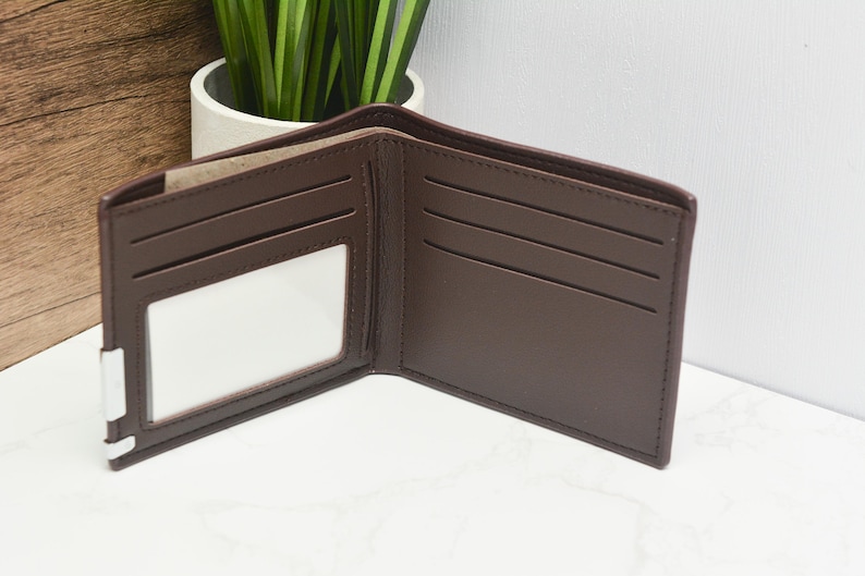 May include: A brown leather wallet with multiple card slots and a clear ID window. The wallet is open and laid flat on a white surface.