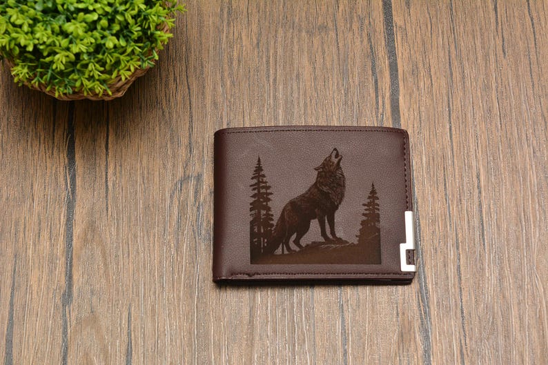May include: Brown leather wallet with a wolf howling at the moon design. The wolf is surrounded by trees and the wallet has a silver metal accent.