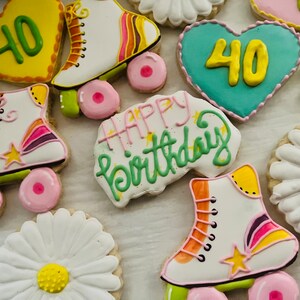 Puede incluir: Surtido de galletas de azúcar decoradas con un mensaje de feliz cumpleaños, diseños de patines y el número 40. Las galletas están decoradas con glaseado de colores y chispas.