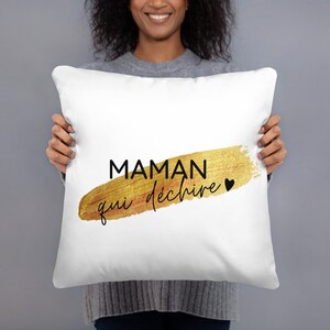 Puede incluir: Almohada blanca con texto dorado y negro que dice "Maman qui déchire" con un pequeño corazón negro.