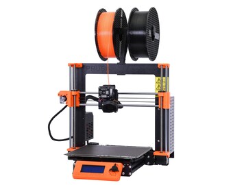 May include: A black and orange 3D printer with a spool of orange filament and a spool of black filament on the top. The printer has a black frame and orange accents. The printer has a small LCD screen on the front. The printer is labelled "PRUSA".