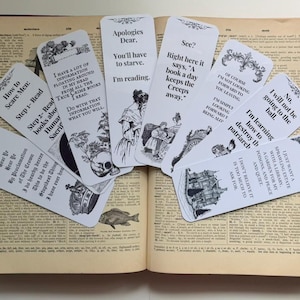 May include: A collection of white rectangular bookmarks with black text and vintage-style illustrations. Each bookmark features unique quotes and decorative borders, fanned out across the open pages of a vintage dictionary with visible text.