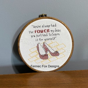 May include: Embroidered hoop art with a quote from the movie "The Wizard of Oz" that reads "You've always had the POWER my dear you just had to learn it for yourself". The quote is surrounded by a yellow brick road design with red ruby slippers.