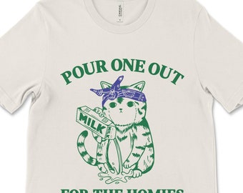 Peut inclure: Un t-shirt blanc avec un motif vert représentant un chat portant un bandana et versant du lait d'un carton. Le texte "POUR ONE OUT FOR THE HOMIES" est imprimé en vert.