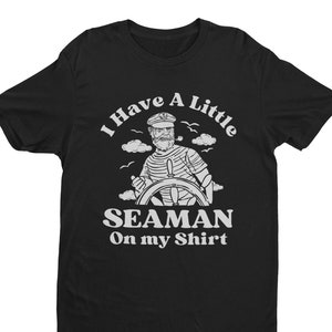 May include: Black t-shirt with a white graphic of a cartoon sailor at the helm of a ship. The text "I Have A Little Seaman On My Shirt" is printed below the image.