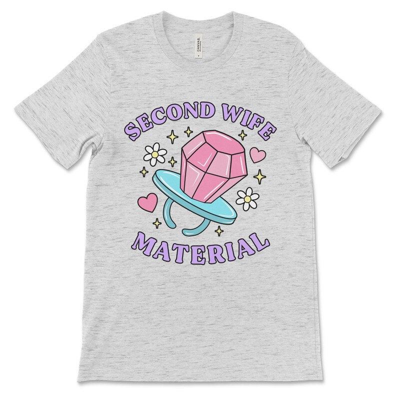 K&ouml;nnte beinhalten: Ein heidefarbenes T-Shirt mit einer lila und pinkfarbenen Grafik eines Diamantrings mit dem Text "Second Wife Material".