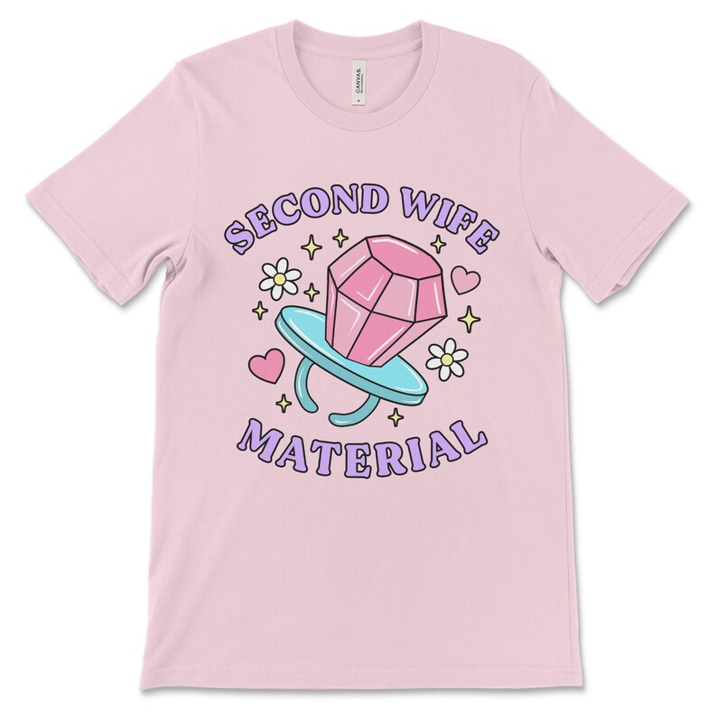 K&ouml;nnte beinhalten: Pinkes T-Shirt mit einer Cartoon-Illustration eines Diamantrings mit dem Text "Second Wife Material" in lila Buchstaben.