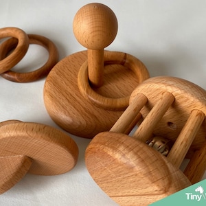 May include: A set of wooden baby toys, including a rattle, a teether, and two rings. The toys are made of natural wood and are designed to be safe for babies.