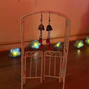 May include: A pair of silver earrings with a black bell-shaped charm and three red bead drops.