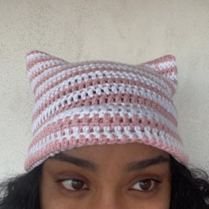 May include: A pink and white striped crocheted hat with cat ears.